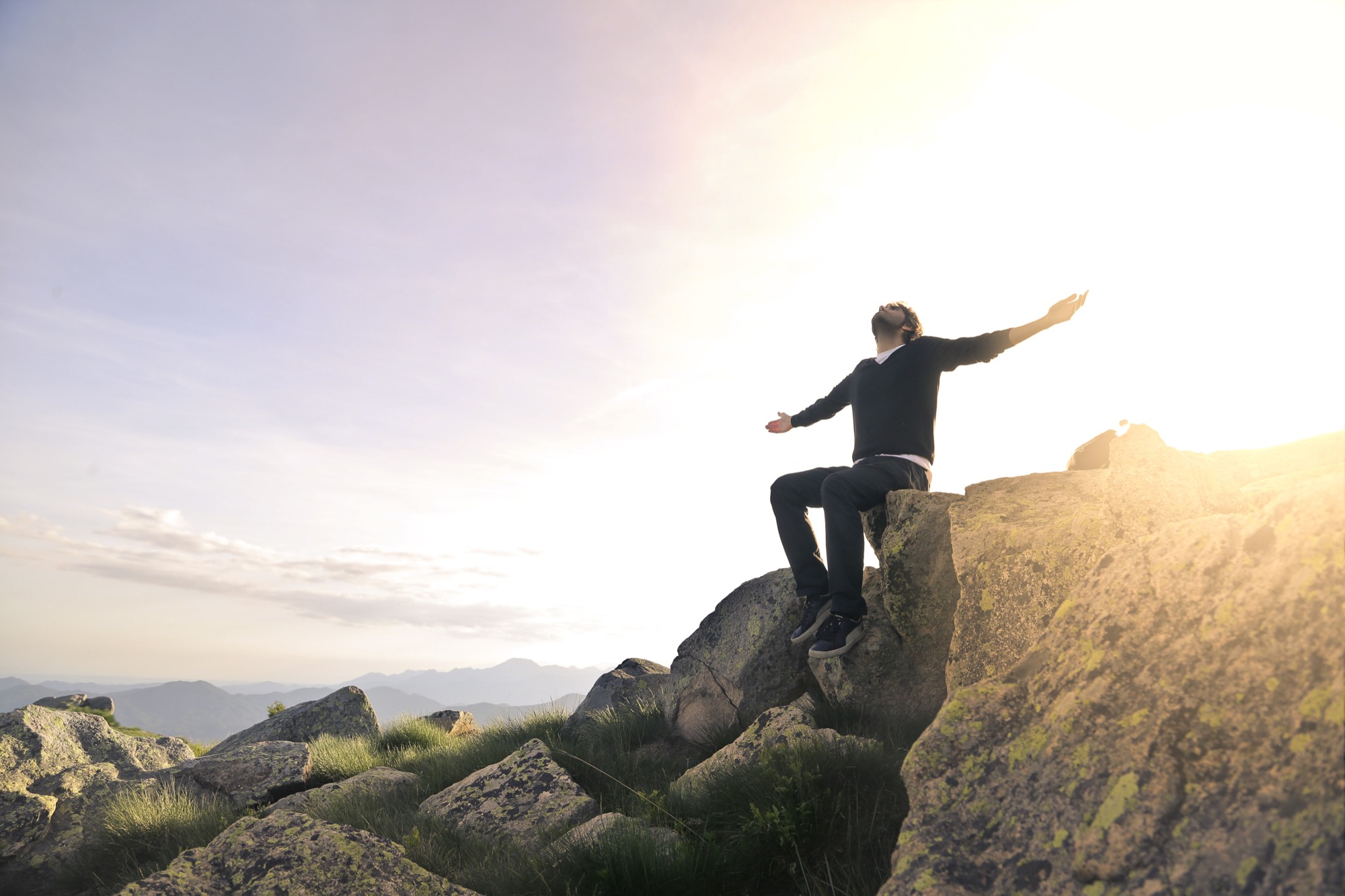 A person standing on a mountain summit at sunrise with arms outstretched